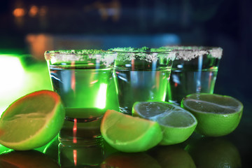 Tequila and limes on a bar counter in green light