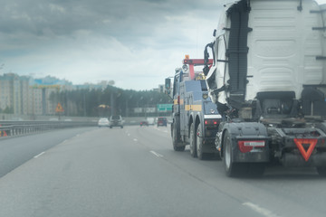 Blue Tow truck delivers the damaged white lorry, Sun light flare, Selective focus. Asphalt highway...