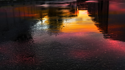 Light and shadows of the night city. Wet asphalt with neon. Soft image of the focus of the street after the rain with reflections on the wet asphalt. Blurred background.