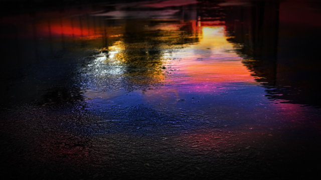 Light and shadows of the night city. Wet asphalt with neon. Soft image of the focus of the street after the rain with reflections on the wet asphalt. Blurred background. © MiaStendal