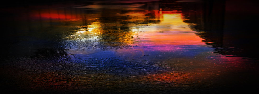 Light and shadows of the night city. Wet asphalt with neon. Soft image of the focus of the street after the rain with reflections on the wet asphalt. Blurred background. © MiaStendal