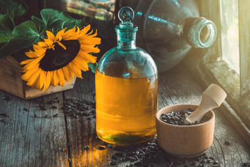 Bottle of sunflower oil, wooden mortar of seeds and yellow sunflower on wooden table.