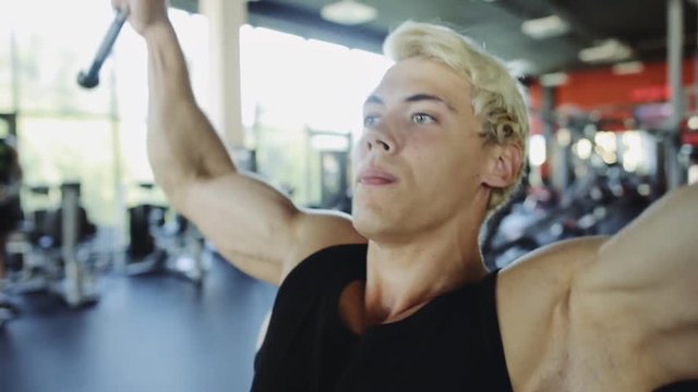 Young sporty man doing excersise on a lat machine in gym close up
