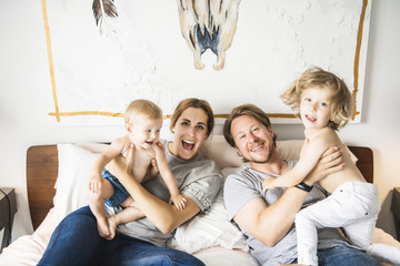 Family of four with baby having fun on bed