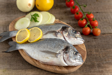 Fresh dorada fish with vegetables on wooden background.