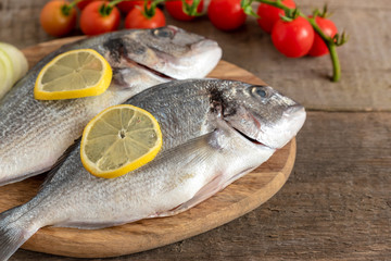 Fresh dorada fish with vegetables on wooden background.
