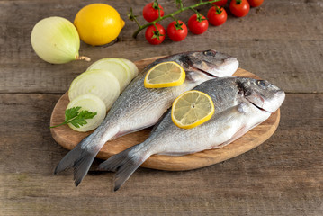 Fresh dorada fish with vegetables on wooden background.