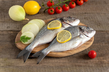 Fresh dorada fish with vegetables on wooden background.