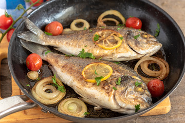 Dorada fried in a pan with onions, lemon and cherry tomatoes