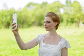 Portrait of smiling beautiful young woman close up with mobile phone, against background of summer green park.