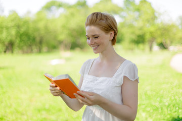 Fototapeta premium serious young, beautiful girl holding an open book, read background summer green park