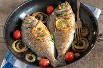 Dorada fried in a pan with onions, lemon and cherry tomatoes