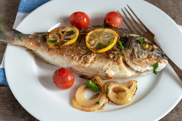 Dorada on plate with onions, lemon and cherry tomatoes