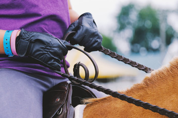 Girl holds reins of horse in black leather gloves
