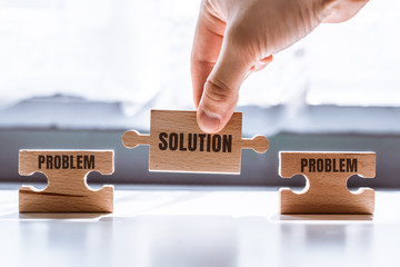 Hand holding a wooden jigsaw puzzle with solution and problem word. There is a matching puzzle next...