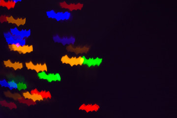 holidays, decoration and party concept - defocused bokeh multicolor lights in shape of bats for halloween background