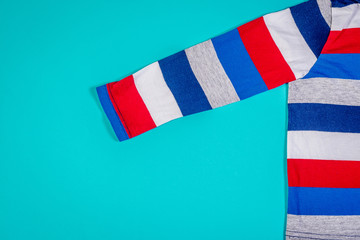 Top view of a children's long-sleeved T-shirt. A shirt with red and blue stripes lies on a turquoise pastel background.