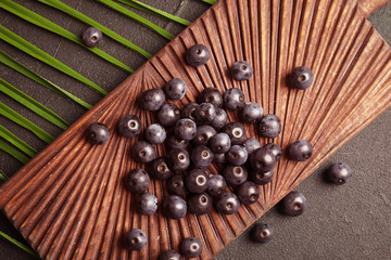 Fresh acai berries on wooden board, top view