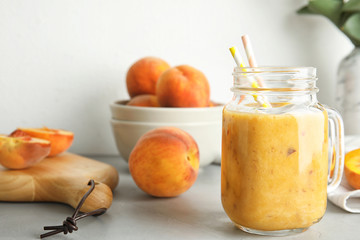 Tasty peach smoothie in mason jar and fresh fruit on table