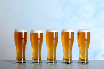 Glasses with beer on table against color background