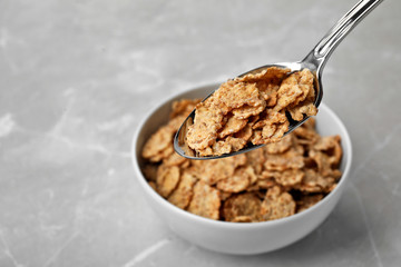Spoon with cornflakes over bowl on table. Whole grain cereal