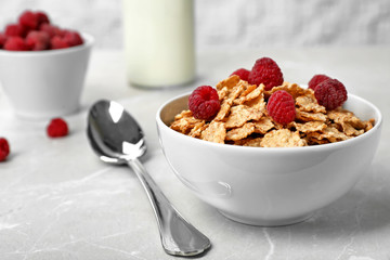 Bowl with cornflakes and raspberries on gray table. Whole grain cereal for breakfast