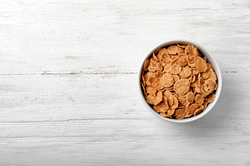 Bowl of cornflakes on light table, top view with space for text. Whole grain cereal for breakfast