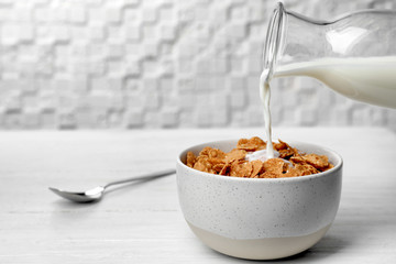 Pouring milk into bowl with cornflakes on light table. Whole grain cereal for breakfast