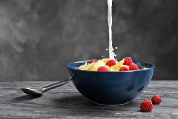 Pouring milk into bowl with cornflakes on dark table. Whole grain cereal for breakfast