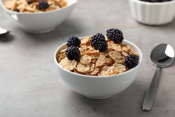Bowl with cornflakes and blackberries on gray table. Whole grain cereal for breakfast