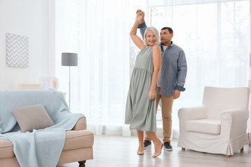 Adorable mature couple dancing together in living room