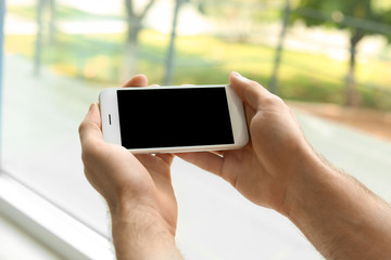 Man holding mobile phone with blank screen on blurred background, closeup. Mockup for design