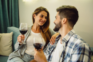 Portrait of a smiling young couple celebrating anniversary with glasses of wine at home on a couch