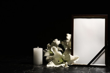 Funeral photo frame, burning candle and lily flowers on dark background