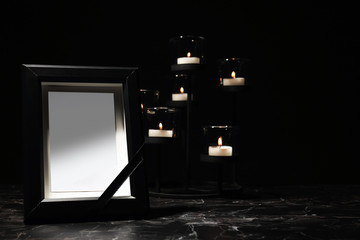 Funeral photo frame and burning candles in holder on dark background