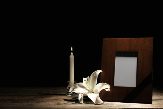 Funeral photo frame, burning candle and white lily on dark background