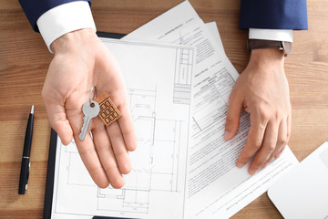 Real estate agent holding key over table in office, top view