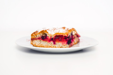 Tasty and fresh rhubarb cake. A piece of cake with red fruit on a white plate isolated on a light, white background. A treat on a plate. Sweet-sour dough.