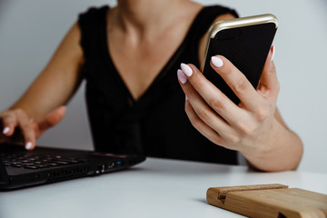 A woman businesswoman is sitting at the computer and works. Work at the laptop. There is a notebook on the desk, the woman checks the information on the phone. Home work concept.