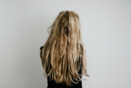A view of the hair from the back of a woman, a girl's figure isolated on a bright gray background. The back of a modern woman dressed in a black blouse and pants, blond fair hair.