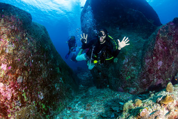 Fototapeta na wymiar A SCUBA diver exiting an underwater tunnel on a deep, dark tropical coral reef