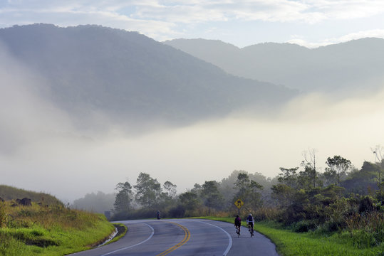 Highway with cyclists, fog, hills and trees