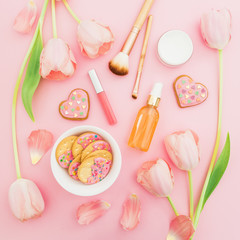 Fototapeta na wymiar Pink flowers, cosmetics and cookies arrangement on pink pastel background. Flat lay, top view
