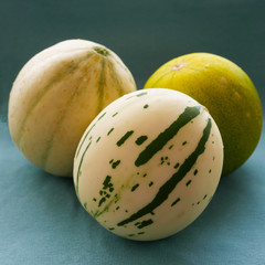 Three different varieties of whole melons arranged on a blue cloth
