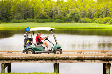 Senior man driving golf cart over water hazard.