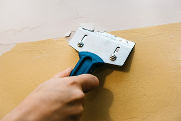 Close-up. A man with a scraper removes the old covering from the wall for further repairs. Wall repair inside the room.