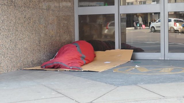 A homeless man in a sleeping bag lying by the office entrance. 