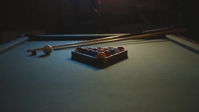A slide in shot of a pool table in a dark basement. The setting is meant to feel cool or edgy.