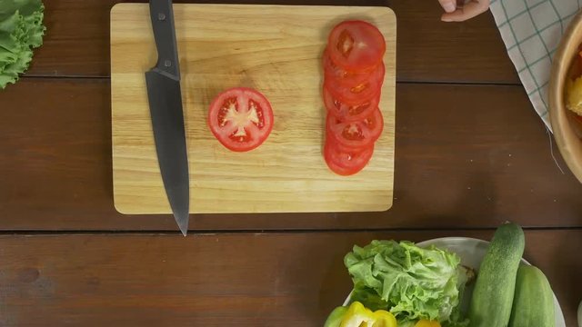 Top view of woman chief making salad healthy food and chopping tomato on cutting board in the kitchen.