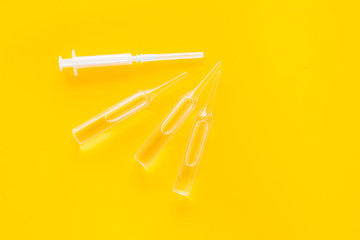 Flu vaccination concept. Syringe and ampoulie on yellow background top view copy space